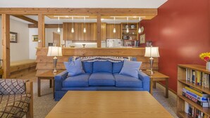 A cozy living room with a blue sofa, wooden coffee table, and a bookshelf filled with books. - RMR: Juniper 112 Condo in The Aspens/Wilson,WY (Wilson)