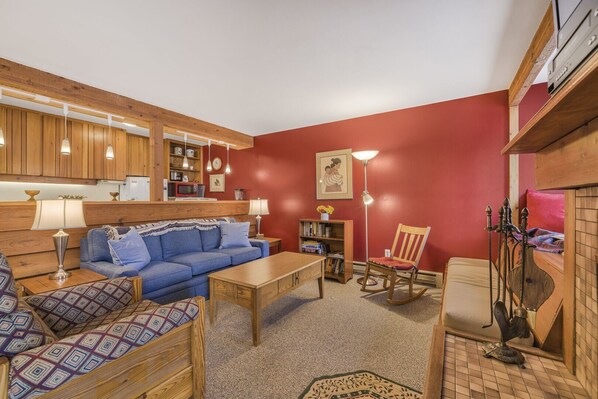 A cozy living room with a blue sofa, wooden furniture, a bookshelf, and a red accent wall.