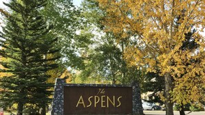 A sign for The Aspens with a stone wall and a mix of green and yellow trees in the background. - RMR: Juniper 112 Condo in The Aspens/Wilson,WY (Wilson)