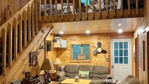 A cozy cabin interior with a wooden staircase, a sofa, a coffee table, and a dining area.