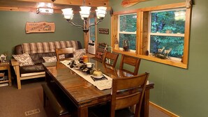 A cozy dining area with a wooden table, chairs, and a bench. There is a window with a view of trees and a sign on the wall.