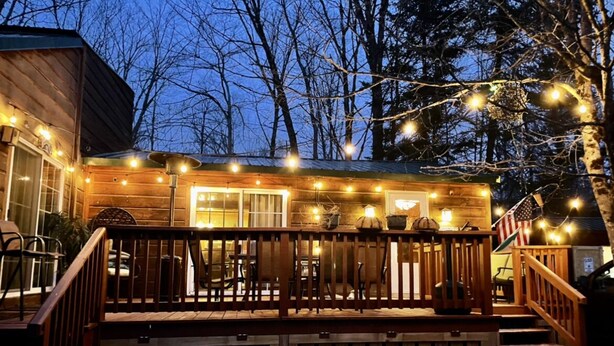 A wooden cabin with a deck, surrounded by trees, and decorated with string lights.