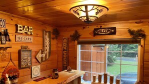 A wooden cabin interior with a bar area, wooden walls, and a window with a view of the outdoors.