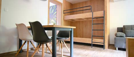 A compact room with a bunk bed, a dining table with chairs, and a small sofa.