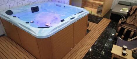 A wellness room with a hot tub, wooden flooring, and a seating area with a table and chairs.