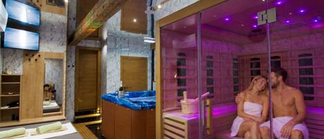 Une salle de sauna avec un banc en bois et une table de massage, un téléviseur et une armoire en bois sur laquelle se trouve une bouteille.