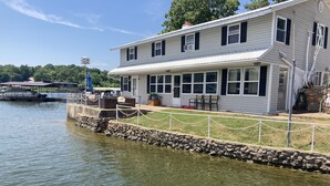 Une maison située au bord de l’eau, dotée d’un quai en pierre, d’un espace salon extérieur et offrant une vue sur l’eau.