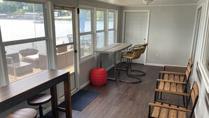 Une pièce avec une table en bois et des tabourets de bar, de grandes fenêtres donnant sur un plan d’eau et une porte menant à l’extérieur.