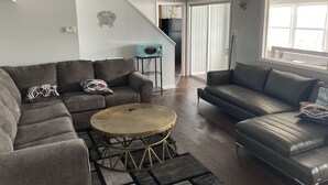 Un salon avec un canapé gris, une table basse ronde et une grande fenêtre qui laisse entrer la lumière naturelle.
