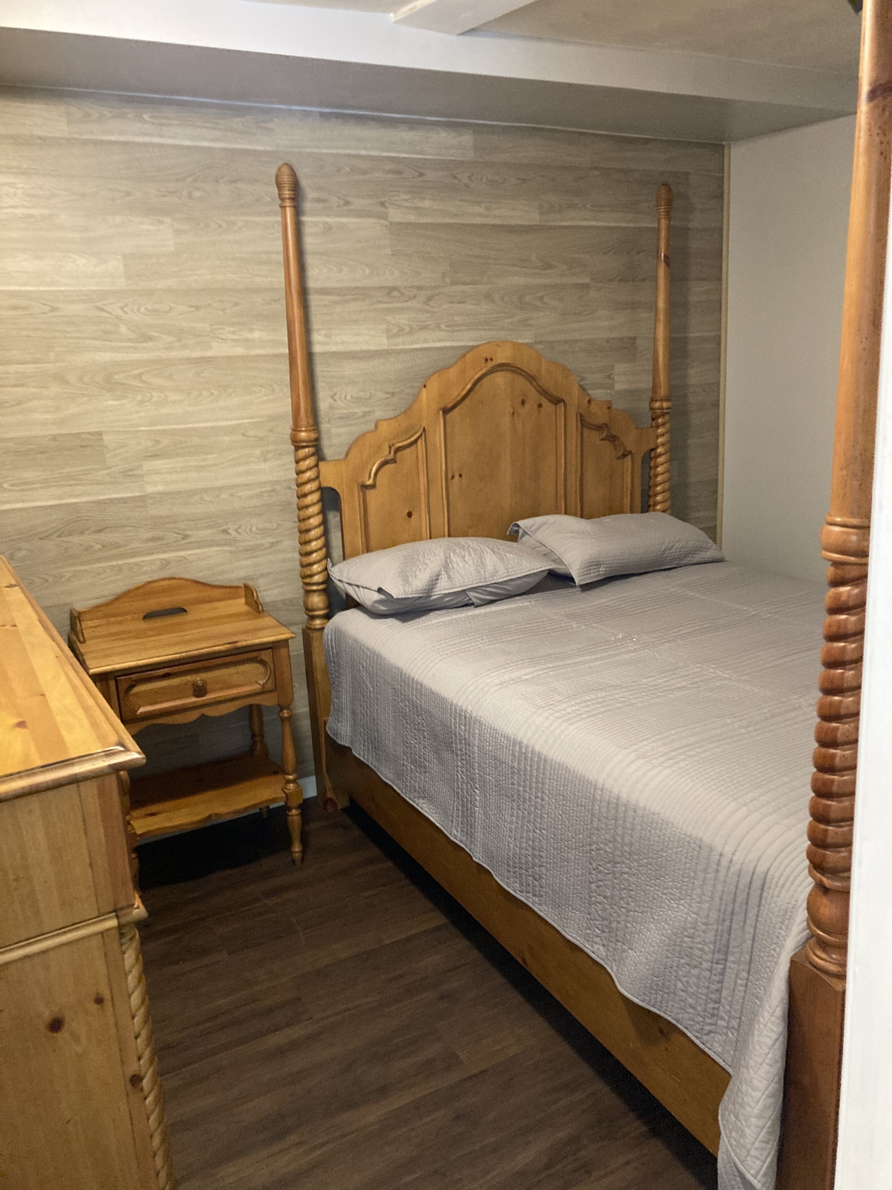 Un lit à baldaquin avec une tête de lit et un pied de lit en bois, une table de chevet avec des tiroirs et une petite table de nuit avec une lampe.
