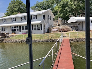 A dock leading to a house with a white exterior and black shutters, a grassy area with a picnic table, and a stone wall. - Lake front with view, dock and calm water (Gravois Mills)