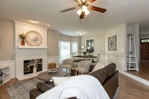 A living room with a fireplace, a ceiling fan, and a dining area with a table and chairs. - Escape to Blue Wilderness: A stylish townhouse (Raleigh)
