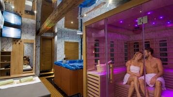 A sauna room with a wooden bench and a massage table, a television, and a wooden cabinet with a bottle on it.
