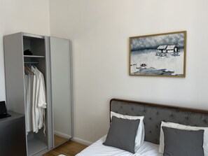 A bedroom with a bed, grey and white pillows, a grey headboard, a wardrobe, and a framed painting on the wall. - Prague National Museum Apartment (Prague)