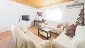 A living room with a wooden ceiling, white walls, a television on a cabinet, a sofa, a coffee table, and a bookshelf. - Cubo's Finca Sanchez Aranda / Private swimming pool / free wifi (Alhaurín el Grande)