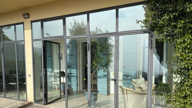 A modern house with large glass doors leading to a patio area with outdoor furniture and potted plants.