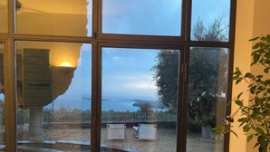A view through a glass door with a stone structure, a paved area, and a distant body of water.