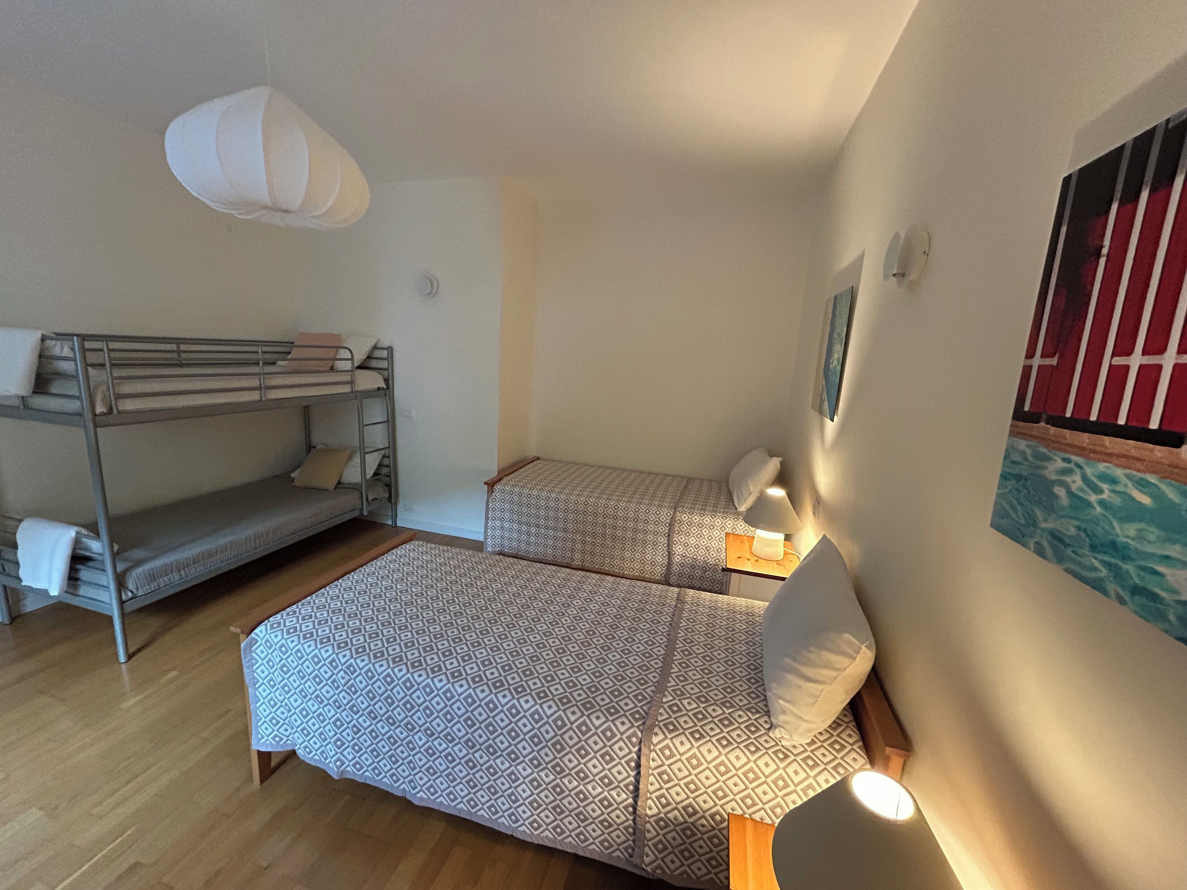 A room with bunk beds, a patterned bedspread, a bedside lamp, and a painting on the wall.