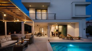 Et moderne hus med to etager, en swimmingpool, udendørs siddepladser og et spiseområde.