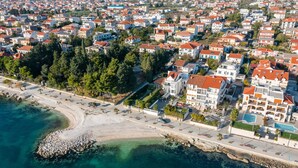 Oversigtsbillede af et kystnært boligområde med huse, en strand og klart, blå vand.