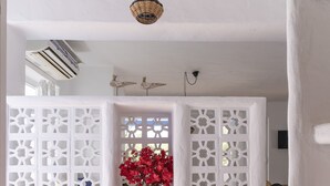 Une cloison blanche agrémentée d’une fenêtre décorative, d’un luminaire suspendu et d’un vase contenant des fleurs rouges.