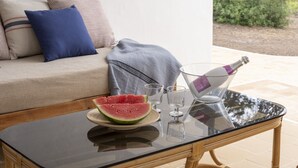 Une table à plateau en verre, une chaise en osier, un canapé en osier avec des coussins et un saladier rempli de tranches de pastèque.