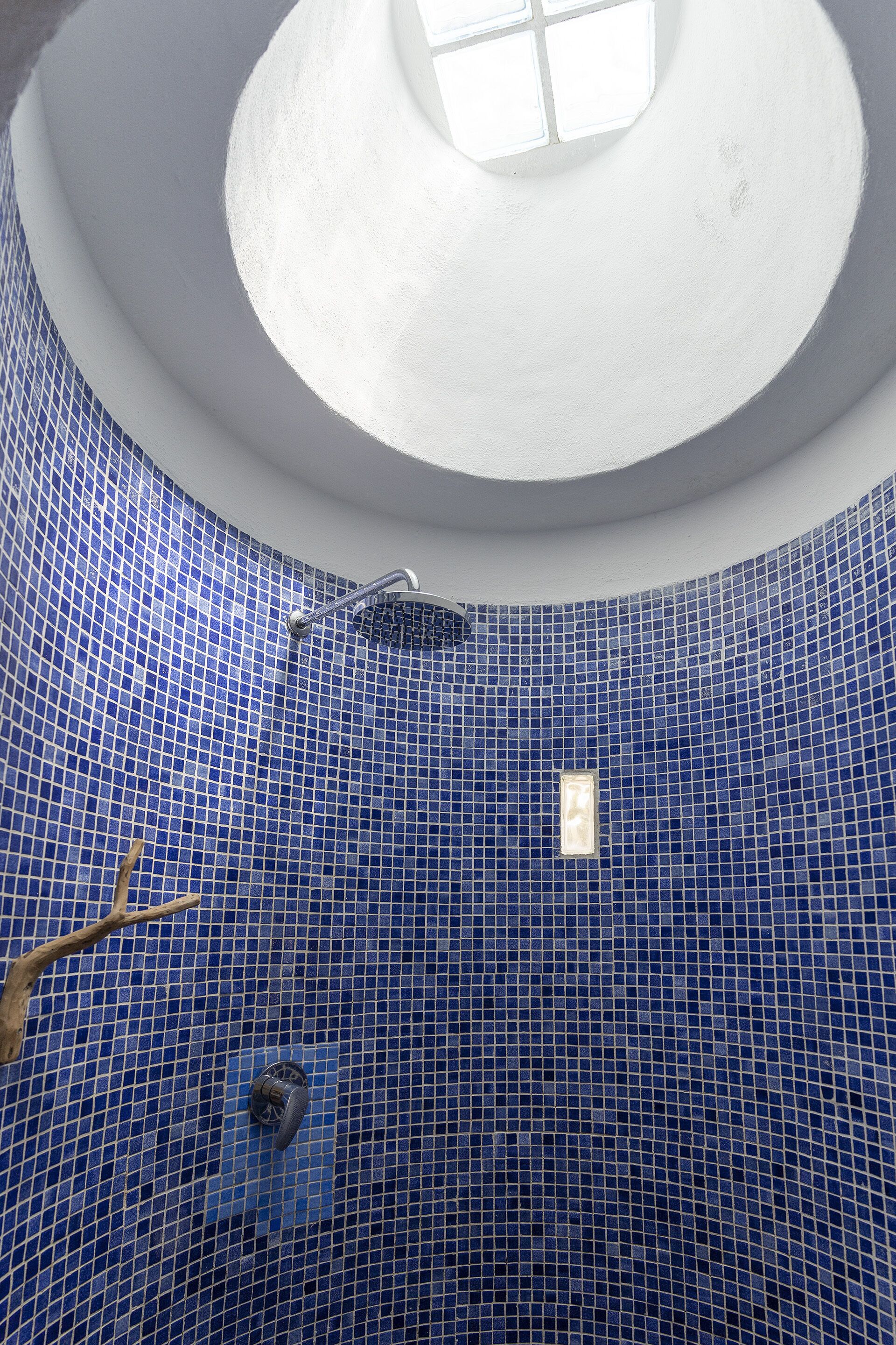 A circular blue-tiled bathroom with a skylight, a shower, and a small window.