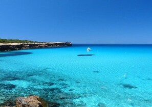 Un paysage côtier avec une eau turquoise et limpide, une côte rocheuse et un bateau au loin.