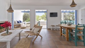 Un vaste espace de vie comprenant une table en bois, des chaises en osier, un canapé et un téléviseur fixé au mur.