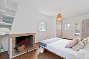 Une chambre avec une cheminée en briques, un lit avec des oreillers, une armoire en bois et un luminaire suspendu.