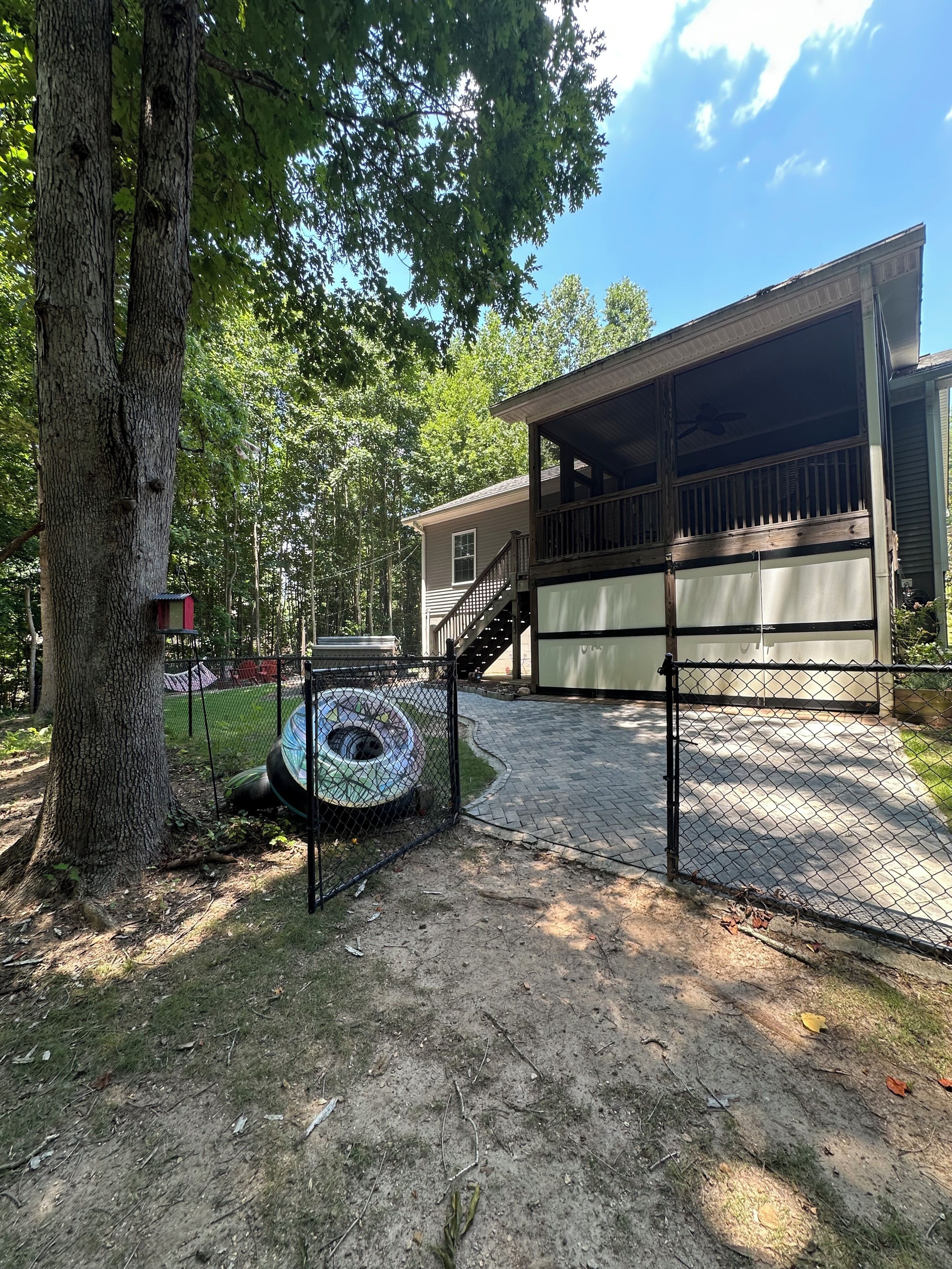 A covered outdoor area with a wooden deck, a fenced-in space with a tire swing, and a house in the background.