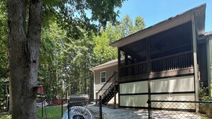 A covered outdoor area with a wooden deck, a fenced-in space with a tire swing, and a house in the background. - Pet-Friendly Lakefront Retreat • Hot Tub, Sandy Shore & Fenced Yard (Westminster)