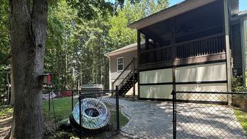 A covered outdoor area with a wooden deck, a fenced-in space with a tire swing, and a house in the background.