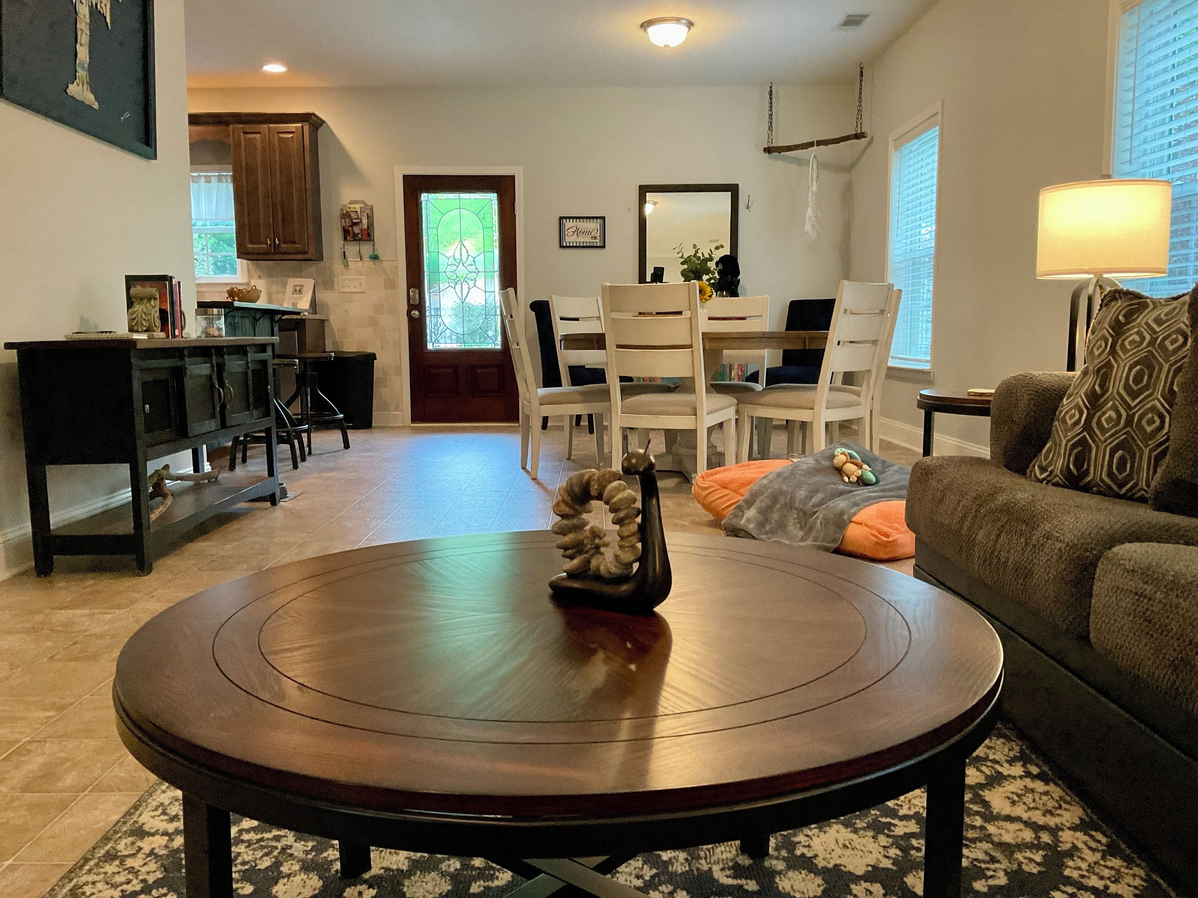 A living room with a round wooden coffee table, a sofa, and a dining area with chairs and a table.