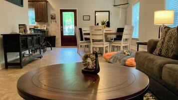 A living room with a round wooden coffee table, a sofa, and a dining area with chairs and a table.