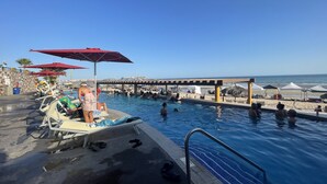 Area piscina con lettini e ombrelloni, una postazione di salvataggio e vista sulla spiaggia e sull'oceano.