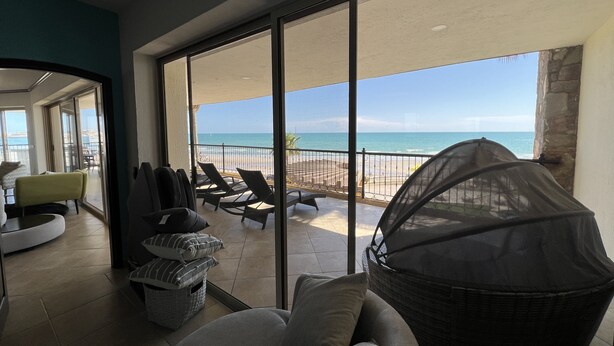 Un balcone con vista sulla spiaggia e sull'oceano, arredato con divano, sedie e una zona salotto coperta.