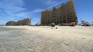 Un hotel sulla spiaggia con diversi balconi e una spiaggia sabbiosa in primo piano.