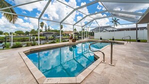 Piscina com água azul cristalina, rodeada por uma área coberta com estrutura de metal e chão revestido de azulejos.