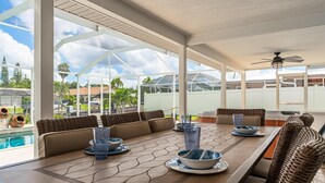 Área de refeições ao ar livre com vista para a piscina, teto branco e mobiliário de vime.