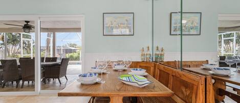 A dining area with a wooden bench and table, glass doors leading to an outdoor patio, and two framed artworks on the wall.