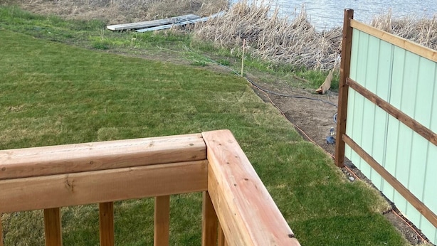 Eine Holzterrasse mit Blick auf einen Fluss, dessen Ufer von Gras gesäumt und im Hintergrund ein Wald zu sehen ist.