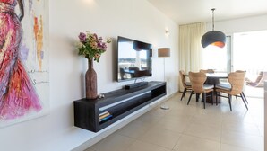 A modern living room with a flat-screen TV, a dining area with wicker chairs, and a large abstract painting on the wall. - Fantastic ocean view apartment on Blue Bay (Sint Michiel)