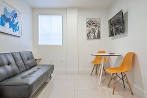 A modern living room with a grey sofa, a small table with two orange chairs, and artwork on the walls. - Miami Suite 206 (Miami)