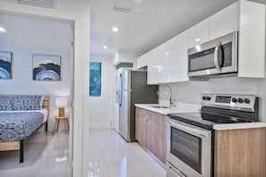 A modern kitchen with stainless steel appliances, a wooden countertop, and a bed with a blue patterned bedspread. - Miami Suite 206 (Miami)