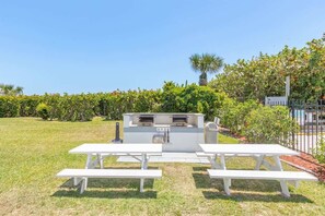 An outdoor barbecue area with a grill and picnic tables. - Poolside Paradise: 2B/2B Oceanfront Complex Steps (Cape Canaveral)