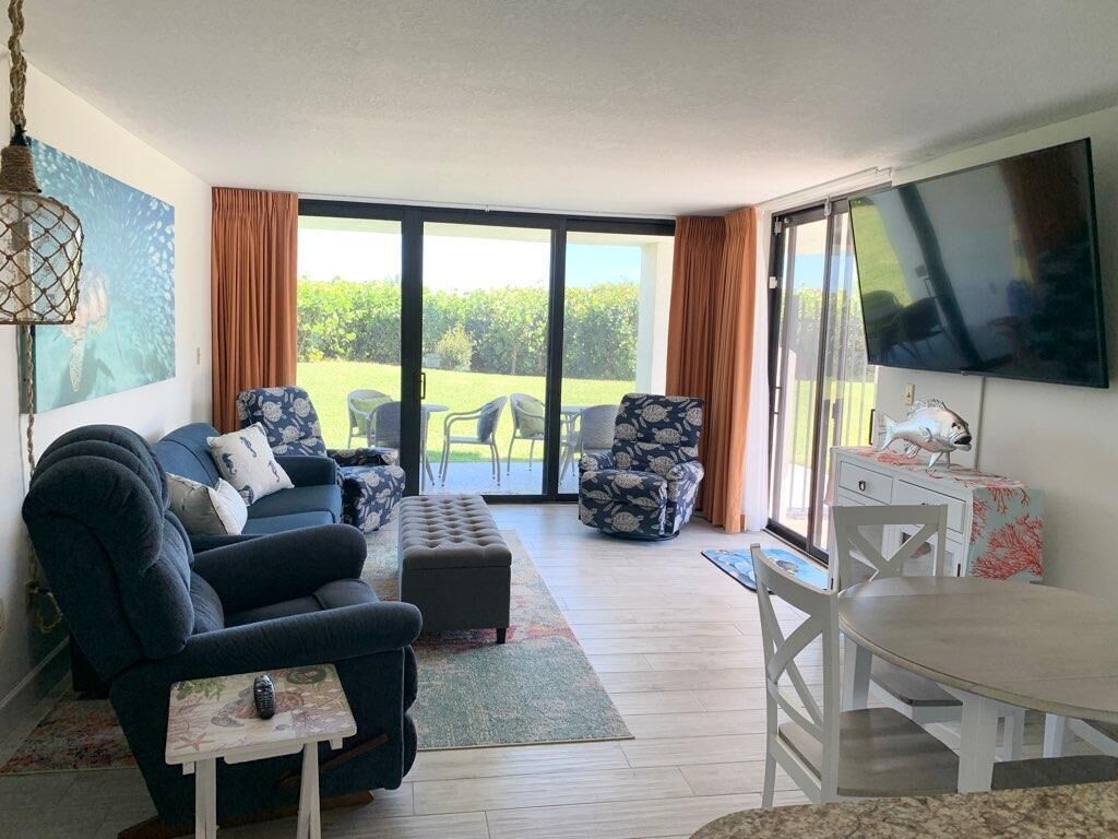 Ein Wohnzimmer mit einer Couch, einem Hocker, Sesseln, einem Esstisch und einem Fernseher.