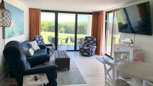 Una sala de estar con sofá, reposapiés y sillas, una mesa de comedor y un televisor.