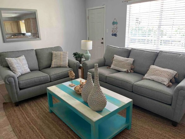 A living room with two grey sofas, a turquoise coffee table, and a mirror on the wall. - Sea La Vie 4 min to Seawall or Cruise Port (Galveston)