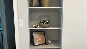 A corner shelf unit with a vase, a framed picture, a small fish figurine, and a potted plant.